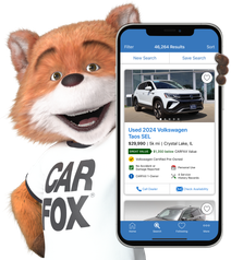 Car Fox smiling showing the CARFAX Car Listings app on a phone.